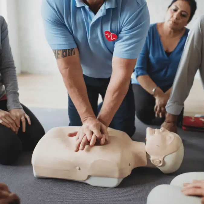 a trainer leads a first aid course by demonstrating cpr on a manaking