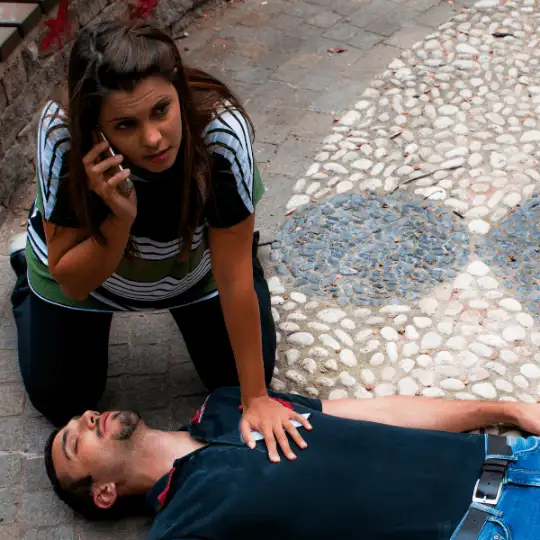 A woman stands over an unconscious patient giving CPR