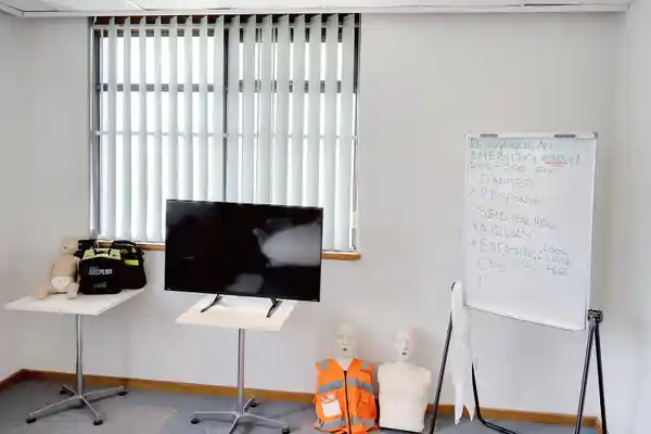 TV, Defibrillator and Whiteboard with DRSABCD action plan in first aid training room.